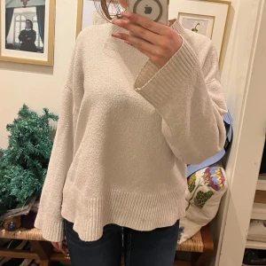 Beige stickad tröja - Mysig beige stickad tröja med långa ärmar och ribbade detaljer vid ärmslut och nederkant. Perfekt för kyliga dagar.