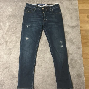 Blå jeans från Jacob Cohen - Snygga blå jeans från Jacob Cohen med slitna detaljer och knappgylf. Tillverkade i Italien med högkvalitativ denim. Perfekta för en stilren look.