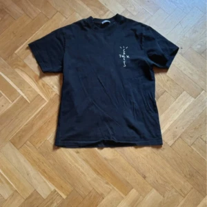 Svart cactus jack t-shirt med tryck 'Look Mom I Can Fly' - Cool svart t-shirt från Cactus Jack med trycket 'Look Mom I Can Fly' på baksidan. Designen inkluderar en bild och text i vitt och rosa. Perfekt för dig som gillar unika och uttrycksfulla plagg.