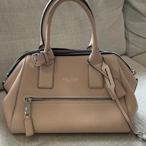 Beige handväska från Marc Jacobs - Elegant beige handväska från Marc Jacobs i skinn med dragkedja och justerbar axelrem. Perfekt för en stilren look. Väskan är nästintill oanvänd så skicket är som nytt!