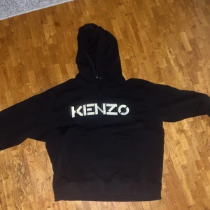 Svart hoodie från Kenzo - Säljer en svart hoodie från Kenzo i bra skick. Den har en stor logga på bröstet och är perfekt för både höst och vinter. Hoodien är bekväm och stilren. Original pris: 3199. Mitt pris: Mycket lägre och kan diskuteras i pm. Rekomenderar Xl till L eller M då oversized passar fint med denna hoodien. Använd en gång