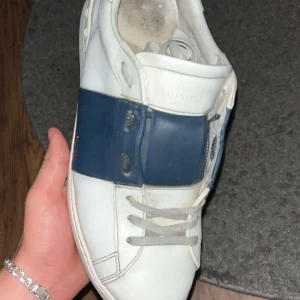 Valentino Garavani sneakers - Snygga Valentino Garavani sneakers i vitt med en bred mörkblå rem över snörningen. Perfekta för en stilren look. Skorna kommer dock inte med box eller påse. Hör av er vid funderingar. Tar emot byter med!!