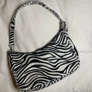 Zebramönstrad axelväska från Bik Bok - Säljer en zebramönstrad axelväska från Bik Bok. Väskan har en dragkedja upptill och är perfekt för att ge din outfit en extra touch!