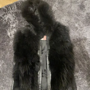 Svart pälsjacka med huva - Säljer en supercool svart pälsjacka med huva. Den är perfekt för vintern och har en lyxig känsla med sitt mjuka pälsmaterial. Jackan har en dragkedja framtill och är i mycket bra skick. Perfekt för att hålla sig varm och stilren under kalla dagar!