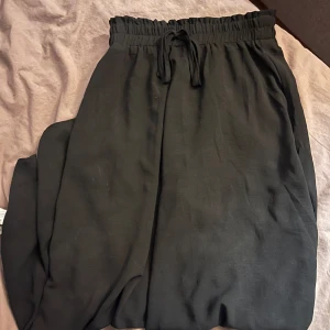 Svarta mjukisbyxor med knytband - Säljer ett par svarta mjukisbyxor i mycket bra skick. De har en bekväm loose passform och är perfekta för avslappnade dagar. Byxorna har ett elastiskt midjeband med knytband för justerbar passform. Perfekta för höst och vintermys!