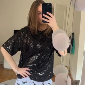 Svart glittrig topp - Säljer en svart glittrig topp som är perfekt för fest! Den har en loose passform och korta ärmar, vilket gör den både bekväm och stilren. Toppen är täckt av paljetter som ger en extra touch av glamour. Perfekt för att lysa upp vilken kväll som helst!  Exempelvis nyår