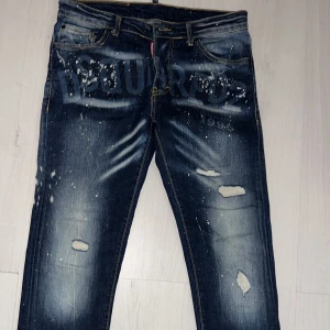 Mörkblå jeans från Dsquared2 - Säljer ett par snygga mörkblå jeans från Dsquared2 med coola slitningar och färgstänk. Har använts max 2 gånger.