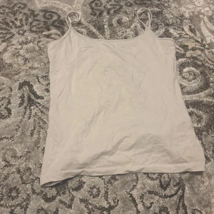 Vit linne topp - Säljer en enkel och stilren vit linne topp med tunna axelband. Perfekt för varma sommardagar eller som ett basplagg i garderoben.