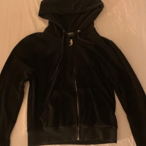 Svart hoodie från Juicy Couture - Säljer en svart hoodie från Juicy Couture i bra skick. Den har en dragkedja framtill och en mysig huva. Perfekt för höst och vår, med långa ärmar och en klassisk passform. Superbekväm och stilren!