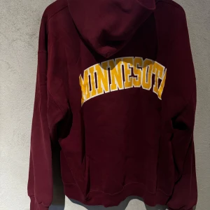 Vinröd hoodie med Minnesota-tryck - Säljer en vinröd hoodie med stort gult Minnesota-tryck på ryggen. Den är vintage och passar som oversize till M. Säljer för 300kr.