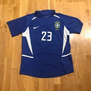 Blå Brasilien fotbollströja kaka - Säljer en blå Brasilien fotbollströja från Nike med nummer 23 och namnet Kaka' på ryggen. Tröjan är från Brasiliens borta tröja från vem 2002. Perfekt för fotbollsfans!