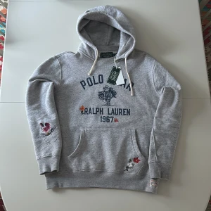 Ralph Lauren Hoddie - Säljer en grå hoodie från Ralph Lauren med broderade detaljer och texten 'Polo Bear 1967'. Den är från POLO Country Club Bear kollektionen och svår att få tag i. Endast testad några gånger med lapp kvar. Nypris: 2499kr Passar dig som är ish 183-195