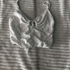 Vit spetslinne - Säljer en söt vit spetslinne med justerbara axelband och knytning framtill. Perfekt för varma sommardagar eller som ett lager under en tröja. Ni sår för frakt 