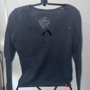 Mörkgrå tröja med knappar från Edc - Snygg mörkgrå tröja från Edc med v-ringning och dekorativa knappar på axeln. Tröjan har långa ärmar och en liten bröstficka med knappdetalj. Perfekt för en stilren look.