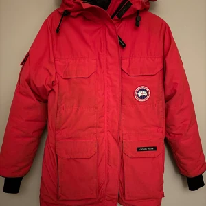 Röd dunjacka Canada Goose - En röd Canada Goose jacka med pälshuva. Expedition Parka. Givetvis äkta. Något skadad i pälsen efter tvätt, se bild. (inlämnad på kemtvätt)