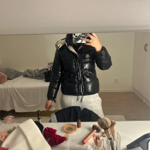 Svart pufferjacka från Moncler - Snygg svart pufferjacka från Moncler med dragkedja och knappar. Jackan har en quiltad design och en praktisk huva. Perfekt för kyliga dagar. Det är en västligt gammal modell där loggan inte går att scanna med telefon och jag har även köpt den begagnad. Inget kvitto. 