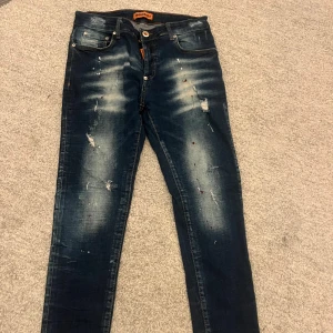 Blå jeans från Dsquared2 - Säljer ett par snygga blå/orange jeans från Dsquared2 med slitna detaljer. Perfekt för fest eller en vardag. Jeansen är i nyskick.