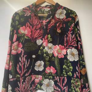 Säljer en superfin blommig blus från H&M i storlek M. Den har ett färgglatt mönster med rosa, vita och gröna blommor på en mörkblå bakgrund. Blusen har långa ärmar och knappar framtill. Lyxig kvalitet och look. Otroligt fint skick. Perfekt för alla tillfällen. 