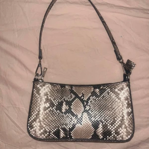 Ormmönstrad axelväska - Snygg axelväska med ormmönster i beige och svart. Perfekt för att ge din outfit en trendig touch. Väskan har en smidig axelrem och är i mycket bra skick💗 skriv för frågor ⭐️