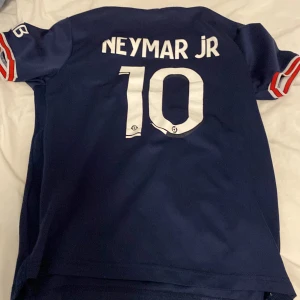 Blå Neymar Jr fotbollströja - Säljer en blå PSG fotbollströja med Neymar Jr och nummer 10 på ryggen. Tröjan har korta ärmar och klubbens emblem på bröstet. Den är i mycket bra skick och perfekt för alla fotbollsfans! 🏆