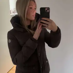 Säljer en snygg brun,grå dunjacka från Moncler i mycket bra skick. Jackan har en hög krage och knappar framtill. Perfekt för kalla vinterdagar med sin varma och mysiga design. Storleken är i S passar en normal passform. Perfekt för både vardag och lite finare tillfällen. Aldrig använd ny pris 10 tusen. Pris går att diskuteras vid snabb affär.