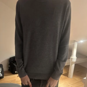 Grå merinoulltröja från These Glory Days - Säljer en stilren och bekväm grå tröja från These Glory Days i Superior Merino. Perfekt för både vardag och lite finare tillfällen. Tröjan har en normal passform och långa ärmar, vilket gör den idealisk för höst och vinter. Supermjuk och håller dig varm! 🐑