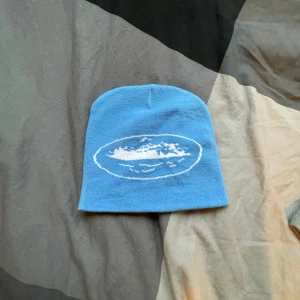 Cortiez mössa - Säljer en snygg blå cortiez mössa. Perfekt för att hålla värmen under kyliga dagar. Mössan är i bra skick och passar de flesta tack vare sin stretchiga passform.