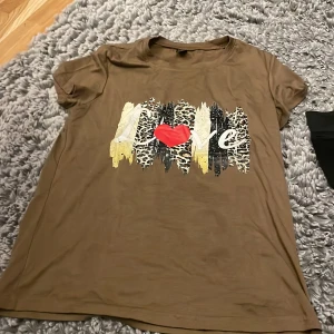 Brun t-shirt med leopardmönster från Shein - Snygg brun t-shirt från Shein med texten 'Love' i leopardmönster och ett rött hjärta på framsidan. Perfekt för en avslappnad stil med korta ärmar och mjukt material.
