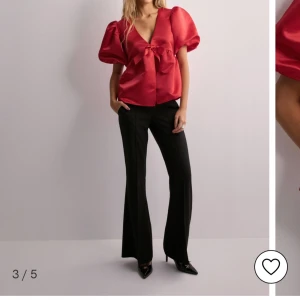 Röd satinblus med rosett - Nelly  - Snygg röd blus i satin med puffiga kortärmar och en v-ringad design. Blusen har en sött rosett framtill som passar perfekt till jul❤️ Helt ny och lappen sitter kvar! Endast testat.