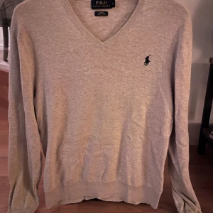 Beige tröja från Polo Ralph Lauren - Säljer en stilren beige tröja från Polo Ralph Lauren i Pima bomull. Tröjan har en v-ringad design och långärmade ärmar med ribbade muddar. Prutat och klart