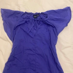 Blå topp från GAP - Snygg blå topp från GAP med korta ärmar och knytning vid halsen. Perfekt för en avslappnad stil. Bara använt en gång och har därför inga skador eller liknade. Skriv gärna om du vore intresserad💙