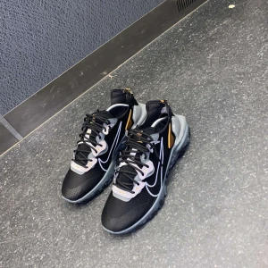 Svarta Nike react vision sneakers med vita detaljer - Snygga svarta Nike sneakers med vita och orange detaljer. Skorna har en modern design med snörning och en bekväm sula. Perfekta för en sportig look.