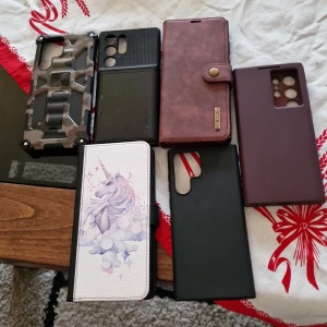 Samling av mobilskal till samsung s22 ultra - En samling av olika mobilskal i varierande stilar och färger. Inkluderar mönster som kamouflage  samt enfärgade alternativ i svart och vinrött. Några skal har detaljer som kortfack och knappar.