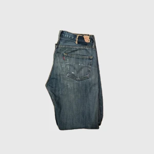 Blå jeans från Levi's - Säljer ett par unika blå jeans från Levis med slitna detaljer och en avslappnad passform. Perfekta för en casual look med en vintage touch. De har  och fem fickor, och är speciella på marknaden. W33 L32. Bara att höra av er vid funderingar eller frågor:)