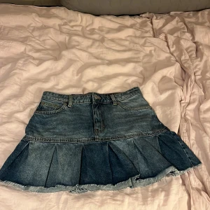 Jeanskjol från Monki - Säljer en superfin jeanskjol från Monki i storlek 40. Kjolen har en cool volangdetalj längst ner och är i en klassisk blå denimfärg. Perfekt för både vardag och fest! 🦋Kjolen är helt ny, en aning ljusare i verklighet än på bilden.