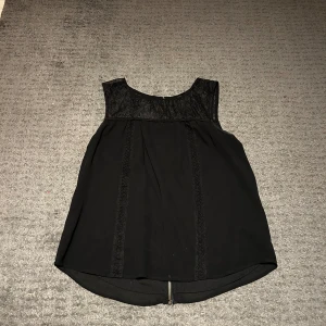 svart mönstrad topp - Snygg svart ärmlös topp med spetsdetaljer upptill. Perfekt för en stilren look. Toppen har en lös passform och rund halsringning.