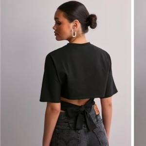 Svart T-shirt- Nelly - Snygg svart croppad topp med korta ärmar och knytning i ryggen. Väldigt populär och oanvänd, storlek S