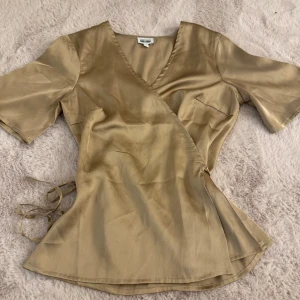 Beige omlottopp från Alexandra Nilsson x BUBBLEROOM  - Snygg beige omlottopp från Alexandra Nilsson x Bubbleboom i storlek 36 (passar både större o mindre då man kan välja hur man vill knyta den på sidan)  Toppen har korta ärmar och en v-ringad design med knytning i sidan. Perfekt för både vardag och festliga tillfällen!