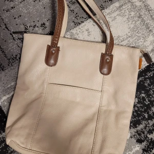 Beige axelväska från David Jones - Snygg vintage beige axelväska från David Jones i syntetmaterial. Väskan har bruna detaljer och dubbla handtag med dekorativa sömmar. Perfekt för att bära med sig det nödvändigaste med stil. Praktisk och vardaglig🌸😊