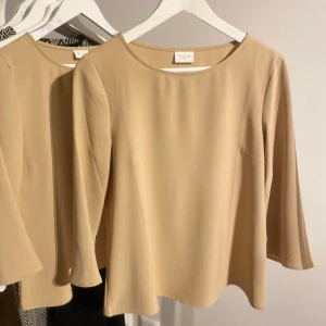 Beige topp från Vila - Säljer en stilren beige topp från Vila med trekvartsärm. Perfekt för en elegant och avslappnad look. Toppen har en rund halsringning och är tillverkad i ett mjukt material.
