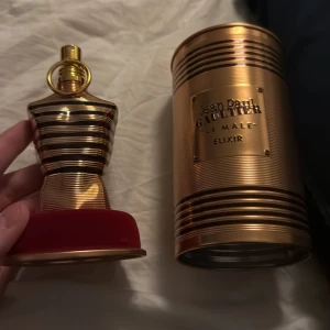 Jean Paul Gaultier Le Male Elixir - Säljer en elegant parfymflaska formad som en manlig torso i guld och svart från Jean Paul Gaultier. Flaskan kommer med en matchande metallförpackning i guld med märkets logotyp. Perfekt för den som vill ha en lyxig doftupplevelse. Den är kvar 75ml i flaskan 