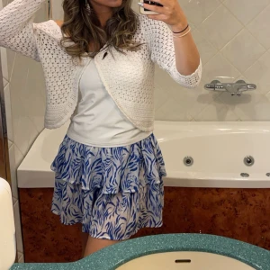 Blå och vit kortkjol med volang - Snygg kortkjol i blått och vitt med ett livligt mönster och volangdetaljer. Perfekt för en somrig look.