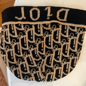 Mönstrad mössa från Dior - Snygg mössa från Dior med ett ikoniskt mönster i svart och beige. Mössan har en elastisk kant med Dior-loggan. Perfekt för att ge en lyxig touch till din outfit.