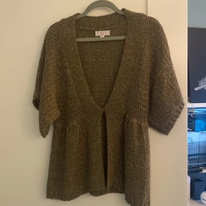 Brun stickad kofta från Gharani Strok - Säljer en brun stickad kofta från Gharani Strok med glittriga detaljer. Koftan har en djup v-ringning och korta ärmar. Den är försedd med en knapp framtill för stängning. Perfekt för att lägga till lite glitter i vardagen.