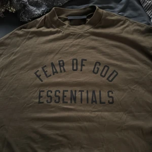 Olivgrön t-shirt från Fear of God Essentials - Snygg olivgrön t-shirt från Fear of God Essentials med tryck framtill. 