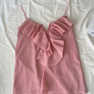 Rosa volanglinne från H&M - Säljer ett sött rosa linne från H&M med smala axelband och volangdetaljer framtill. Postar inom 24h efter köp!🎀Några trådar har gått upp vid spännerna så det sitter en säkerhetsnål där men inget som syns eller känns alls. 💞