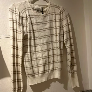 Vit och beige randig tröja från Neo Noir - Snygg vit tröja från Neo Noir med beigea ränder. Tröjan har långa ärmar och en rund halsringning. Perfekt för en stilren look.