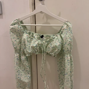 Blommig grön blus med puffärmar - Söt blommig grön blus med puffiga långa ärmar och knytning framtill. Perfekt för en somrig look med sitt lätta och luftiga material.