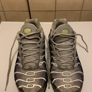 Nike Air Max Plus Tn i grått och svart - Säljer ett par Nike Air Max Plus Tn sneakers i grått och svart med vita detaljer. Skorna har en unik design med vågformade linjer och en synlig Air Max-dämpning i sulan. Perfekta för en sportig look.