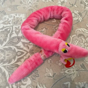 Mjukis orm - Mysig och lekfull ormformad  orm  i lila plyschmaterial. .ormen  har stora gula ögon och en röd tunga som sticker ut.den sätteri fast på sin svans ,som barnen kan hänga rund  axlar eller hur dem vill . Svensk tillverkat frå år 1988 . Maskintvätt 30grader så bra kvalitet . Perfekt som en rolig inredningsdetalj eller som en mjuk leksak.längd är 1,24cm